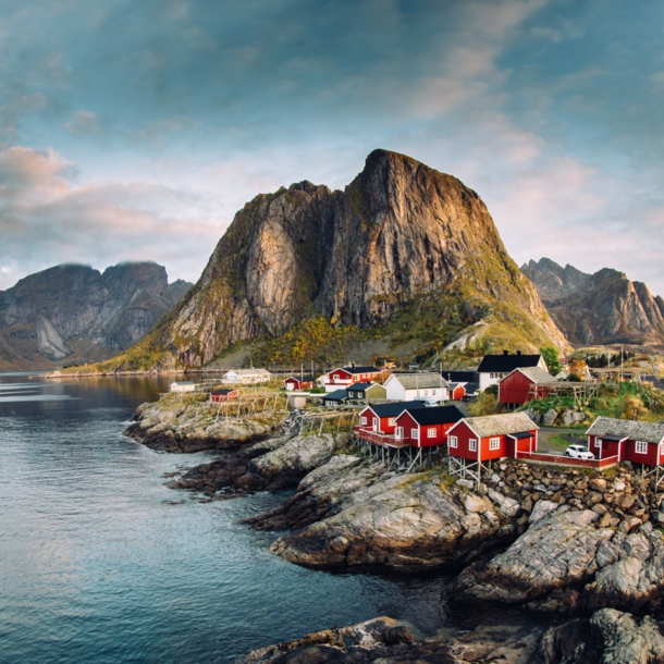 Luftansicht eines Fjords auf den Lofoten mit Felsen, roten Fischerhütten und Bergen.